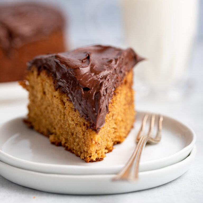 slice of peanut butter cake on a stack of white plate on a grey surface with more cake and a glass of milk in the background