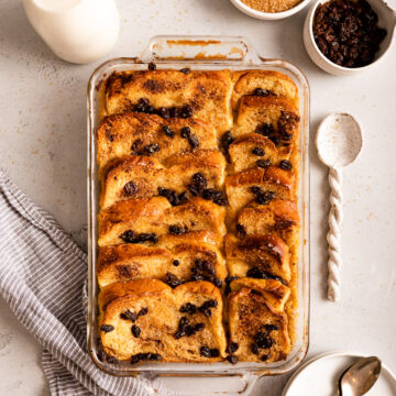 bread and butter pudding, glass of milk, plates and spoons on a light grey background