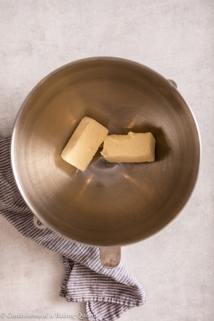 butter sticks in a metal mixing bowl on a light grey surface with a blue and white linen