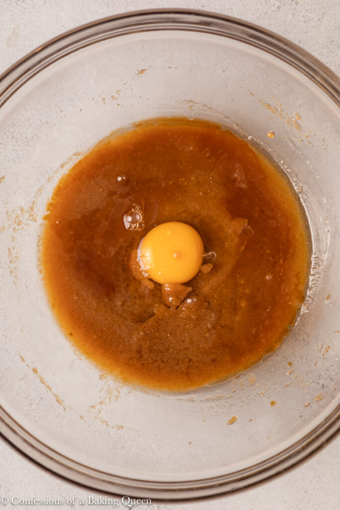 up close of egg and vanilla aded to butter sugar mixture in a glass bowl on a light grey surface
