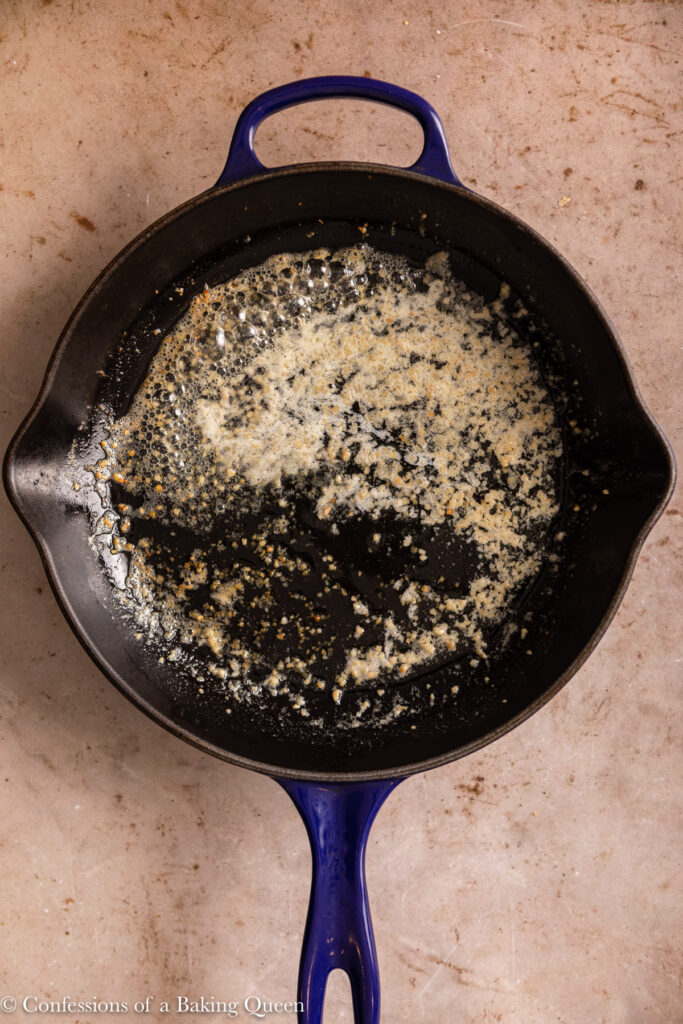 butter and garlic simmering together in an enamel lined cast iron skillet on a light brown surface