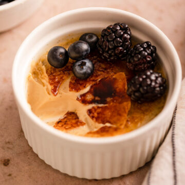 coffee creme brulee with berries half eaten next to a bowl of blueberries and a white and blue stripped on a light brown surface