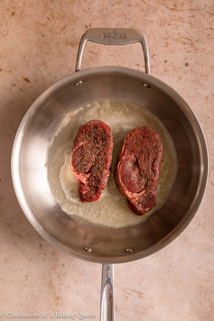 filet mignon cooking in a metal pan with oil and butter on a light brown background