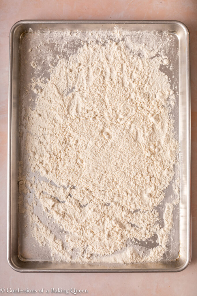 flour spread out on a metal sheet pan on a light pink surface