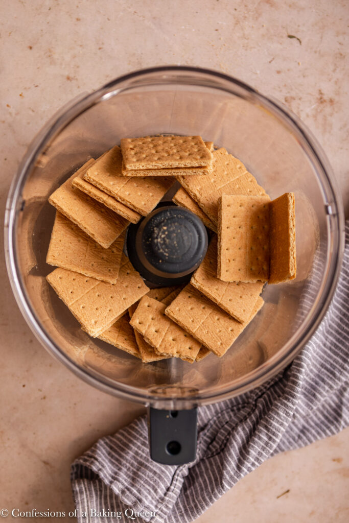 graham cracker biscuits in a food processor on a light brown surface with a blue linen