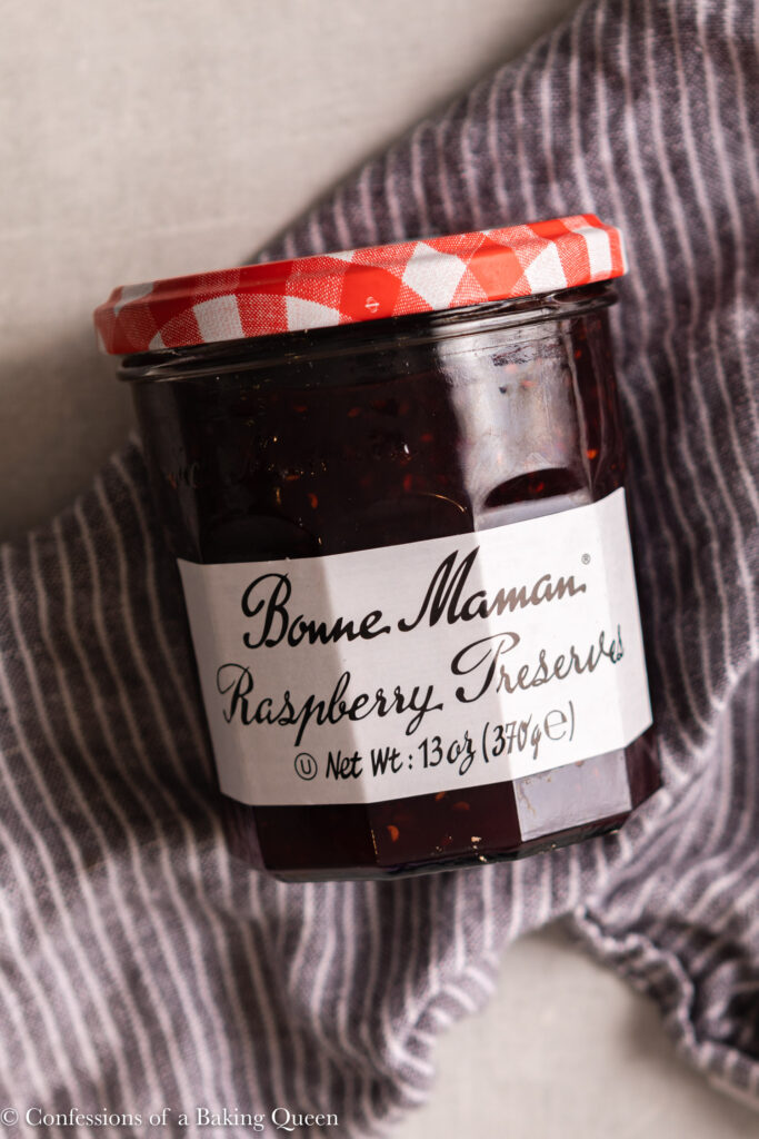 jar of raspberry preserves on a blue linen on a light grey surface