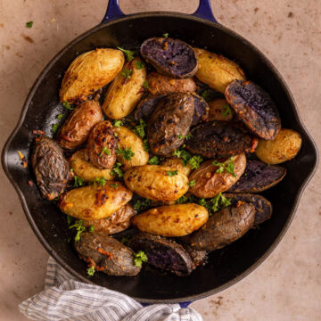 roasted fingerling potatoes in a cast iron skillet with a white and blue linen on a light brown surface