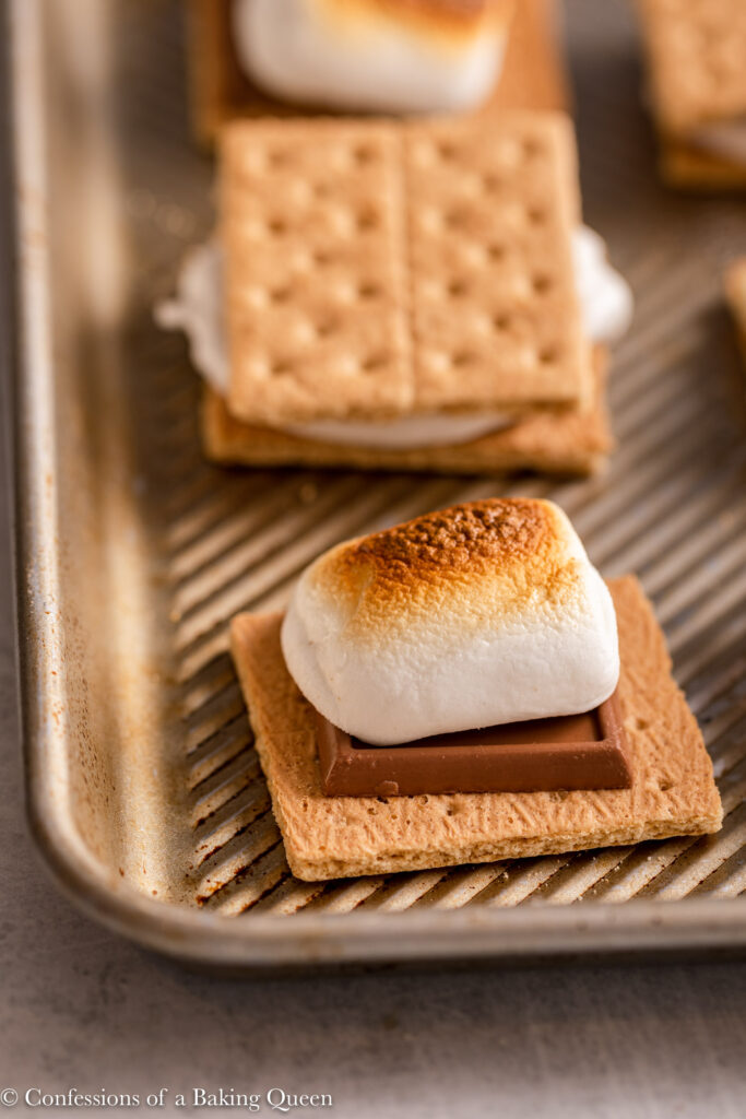 toasted marshmallow on top of chocolate and a graham cracker on a metal baking pan on a light grey surface