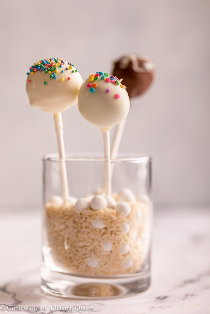 cake pops in a cup filled with rice and pie weights on a white background