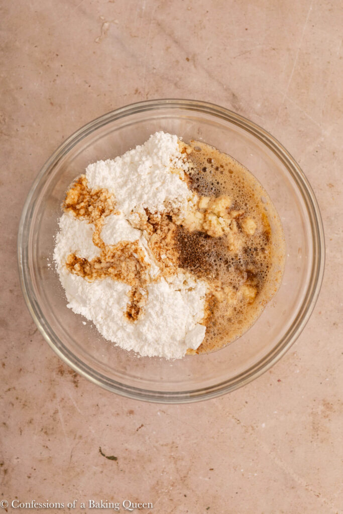 confectioner sugar, brown butter, vanilla bean paste and heavy cream mixed together in a glass bowl on a light brown surface