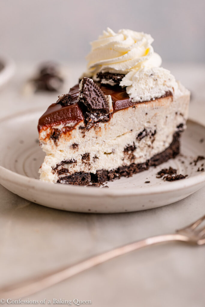 slice of oreo cheesecake on a white plate next to a fork on a marble surface