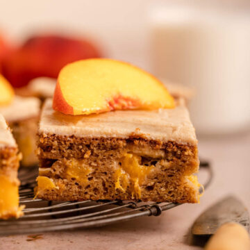 slice of peach on top of a peach cake on a wire rack next to a knife on a light brown surface