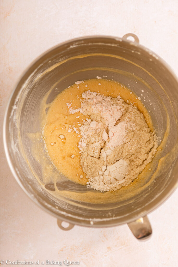 almond flour and custard powder added to wet ingredients for frangipane in a metal mixing bowl on a light surface