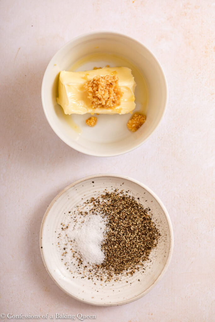 butter and minced garlic in a bowl and a plate of salt and pepper on a light cream surface