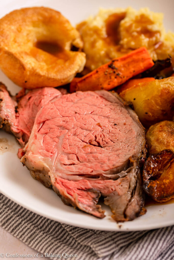close up of medium rare rib eye roast on a roast dinner plate with lots of vegetables