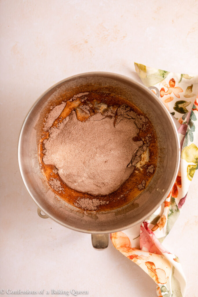 dry ingredients added to wet ingredients in a metal bowl on a light cream surface with a floral linen