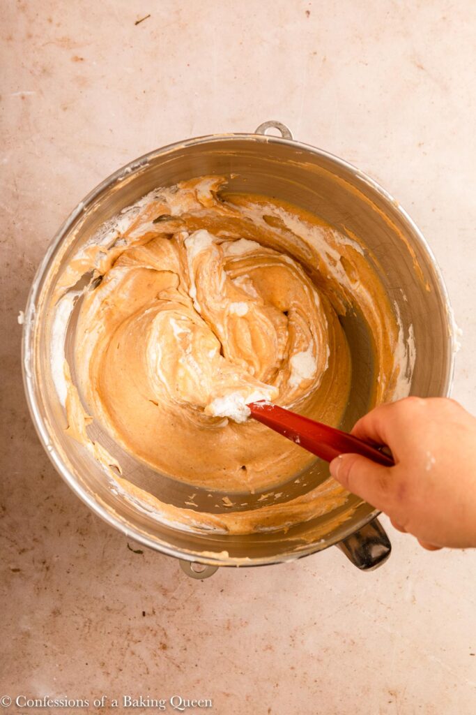 hand folding whipped cream into pumpkin cheesecake batter on a light brown surface