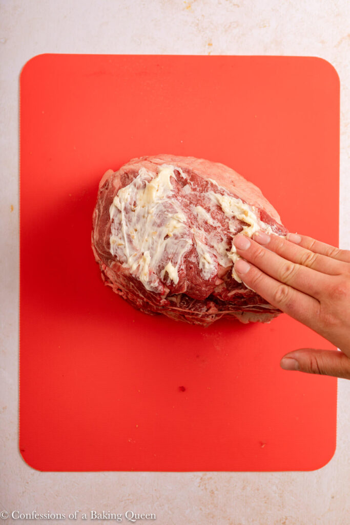 hand rubbing butter and garlic mixture on top raw beef ribeye roast on a light cream surface