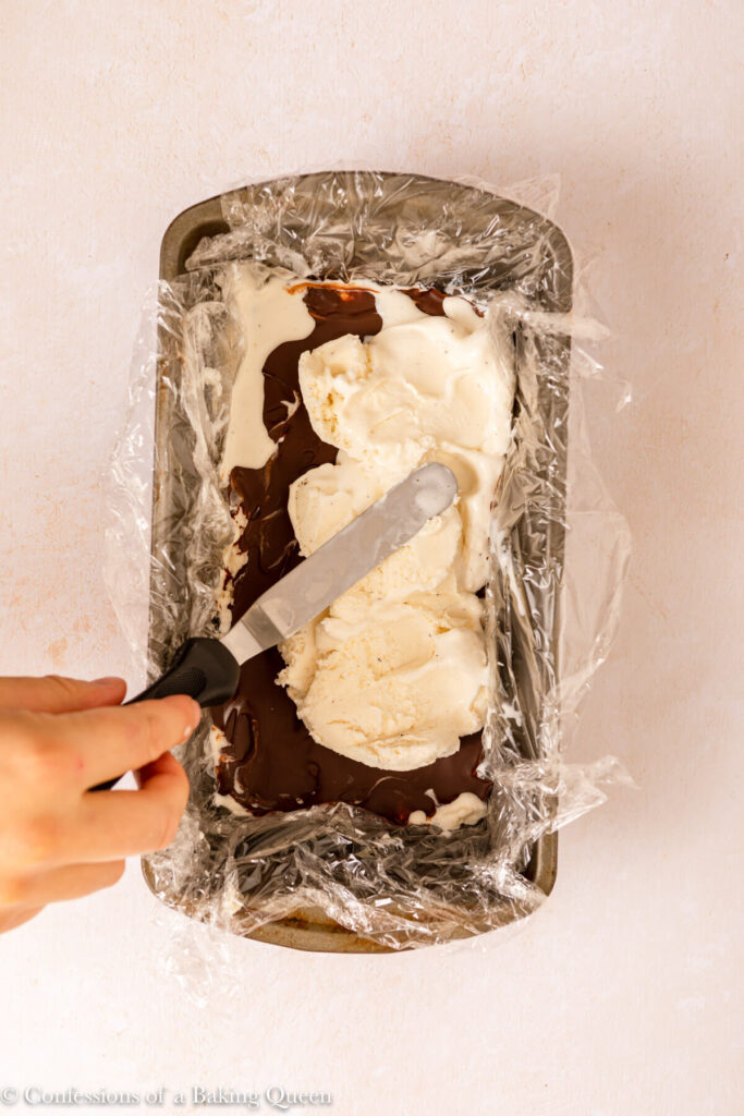 ice cream spread on top of hardened chocolate shell layer in a loaf pan on a light cream surface