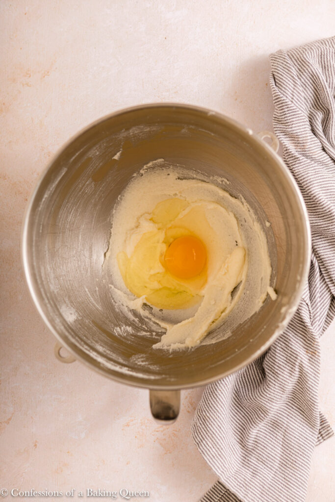 light and fluffy butter and sugar in a metal bowl with an egg in a metal mixing bowl on a light surface with a blue and white linen