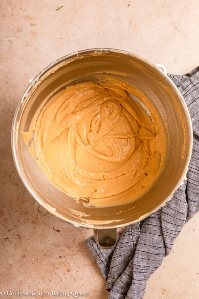 pumpkin cheesecake batter in a metal mixing bowl on a light brown surface with a blue linen