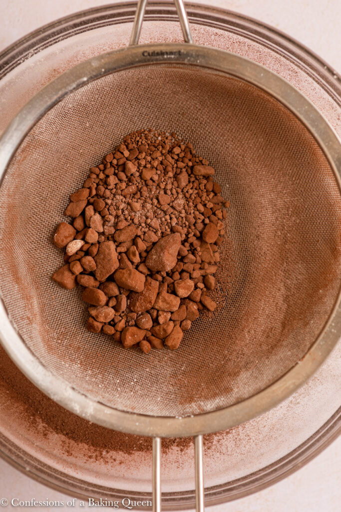 up close of cocoa powder lumps in a metal sieve on a light cream surface