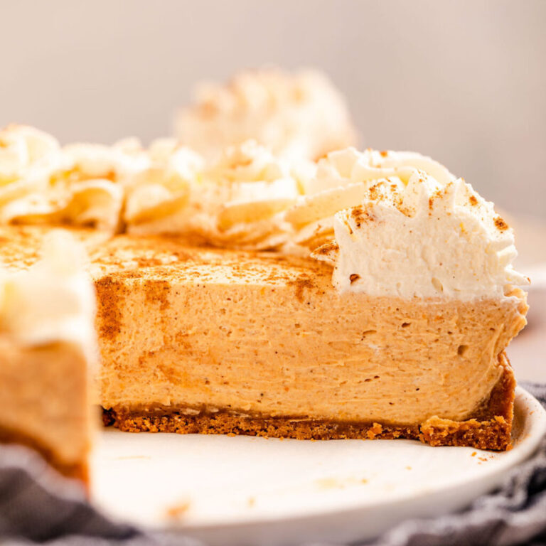 close up of cut open pumpkin cheesecake on a white platter on top of a blue linen on a light brown surface