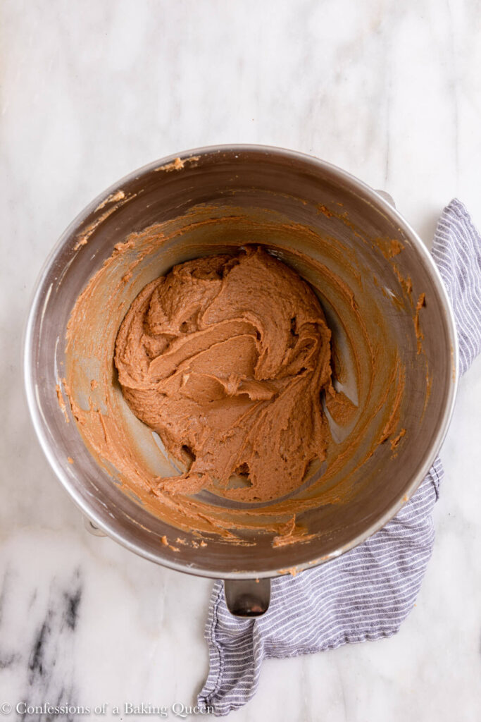 chocolate peanut butter mixture in a metal bowl on a white marble surface with a blue linen