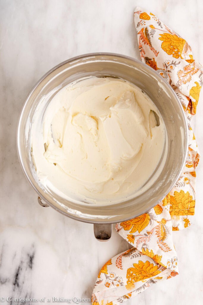 cream cheese mixed until light and fluffy in a metal mixing bowl on a white marble surface with a yellow floral linen