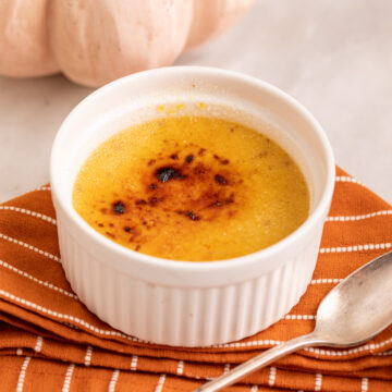 pumpkin creme brulee served next to a pumpkin on a white marble surface with an orange linen