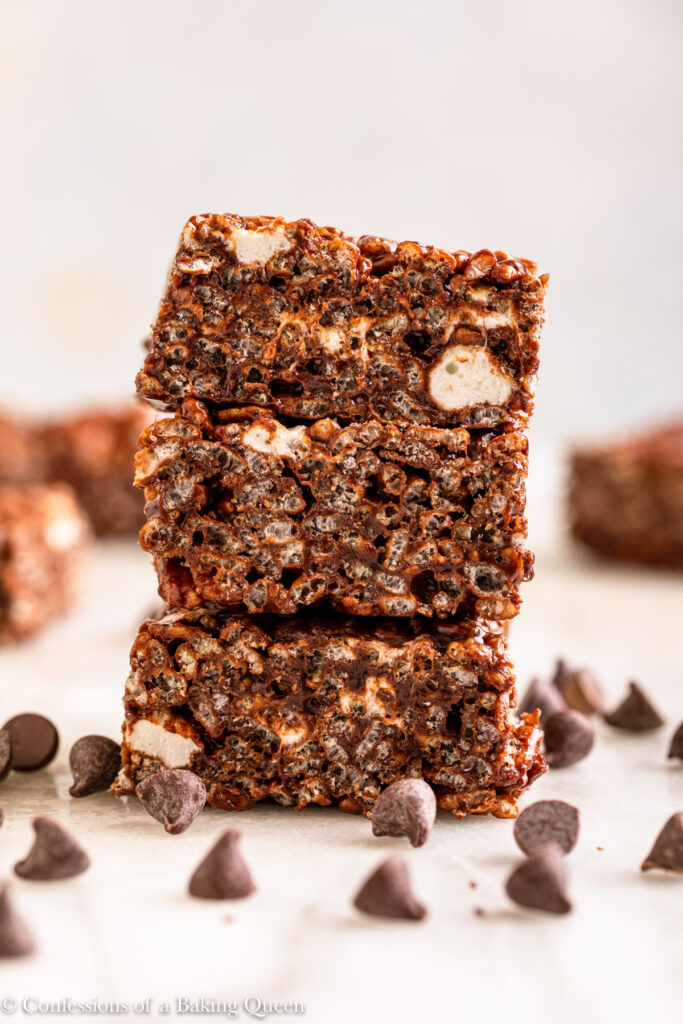 stack of three chocolate rice krispies on top of each other on a white marble surface with chocolate chips