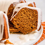 up close of sliced pumpkin bundt cake on a white plate on top of an orange linen on a light grey surface