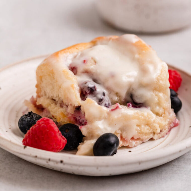 berry sweet roll served on a white plate with a few more berries on a light grey surface