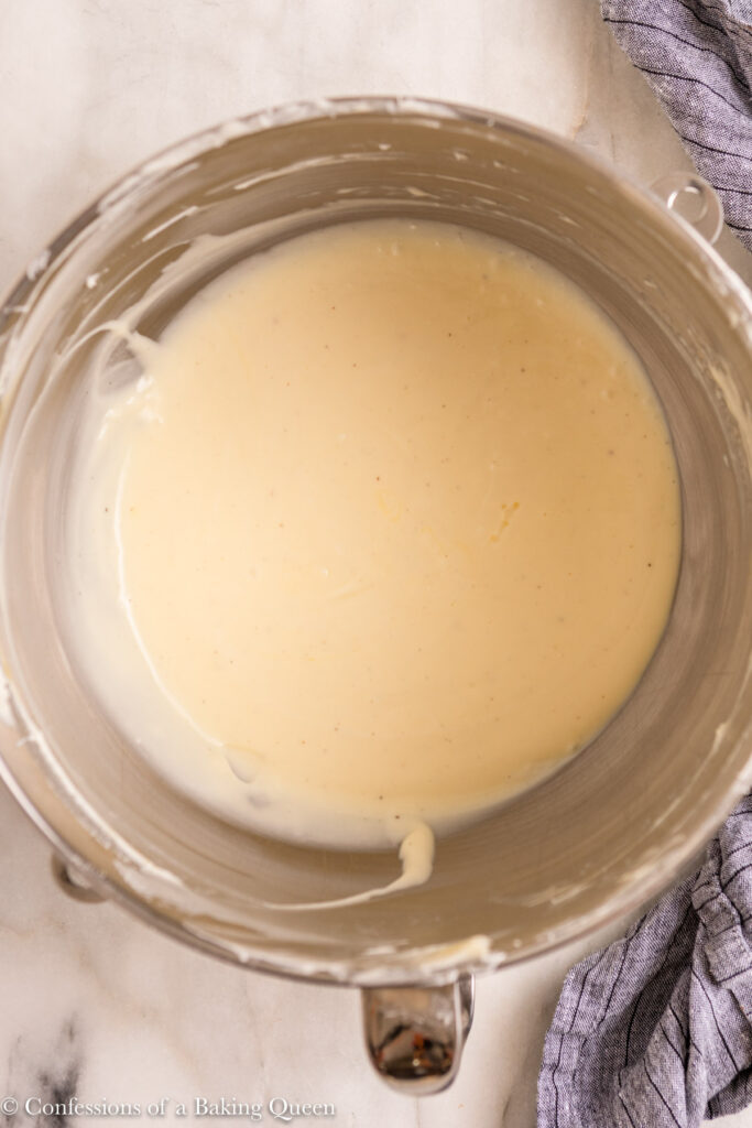 cheesecake batter in metal mixing bowl on a white marble surface with a blue linen