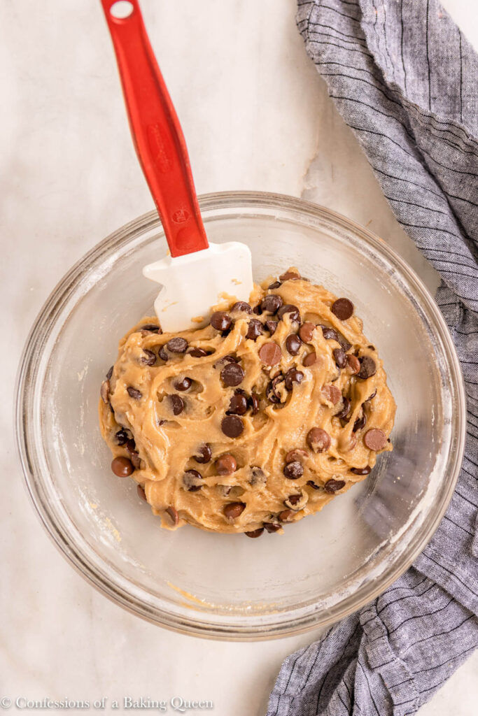 chocolate chip cookie dough in a glass bowl on top of a blue linen on a white marble surface