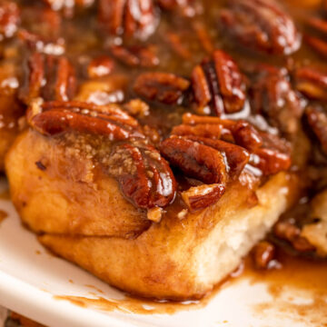 close up of caramel pecan sticky buns on a white platter on top of a yellow floral linen on a light brown surface