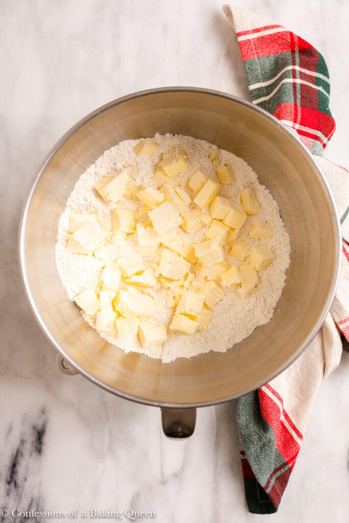 cubed butter added to dry ingredients in a metal bowl on a marble surface with a Christmas linen
