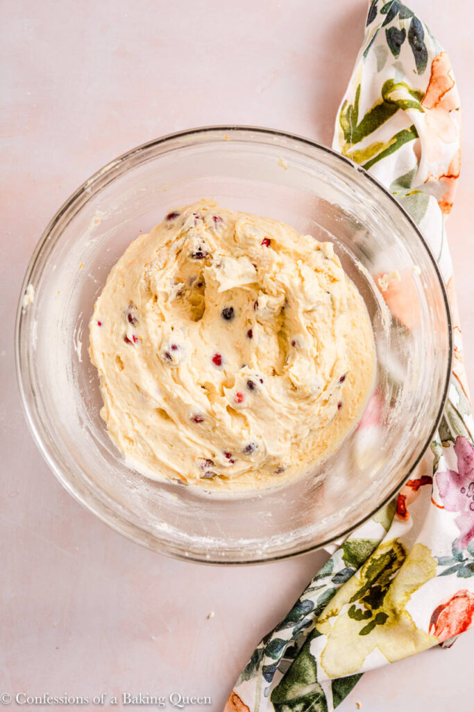 orange cranberry cake batter in a glass bowl on a light pink surface with a floral linen