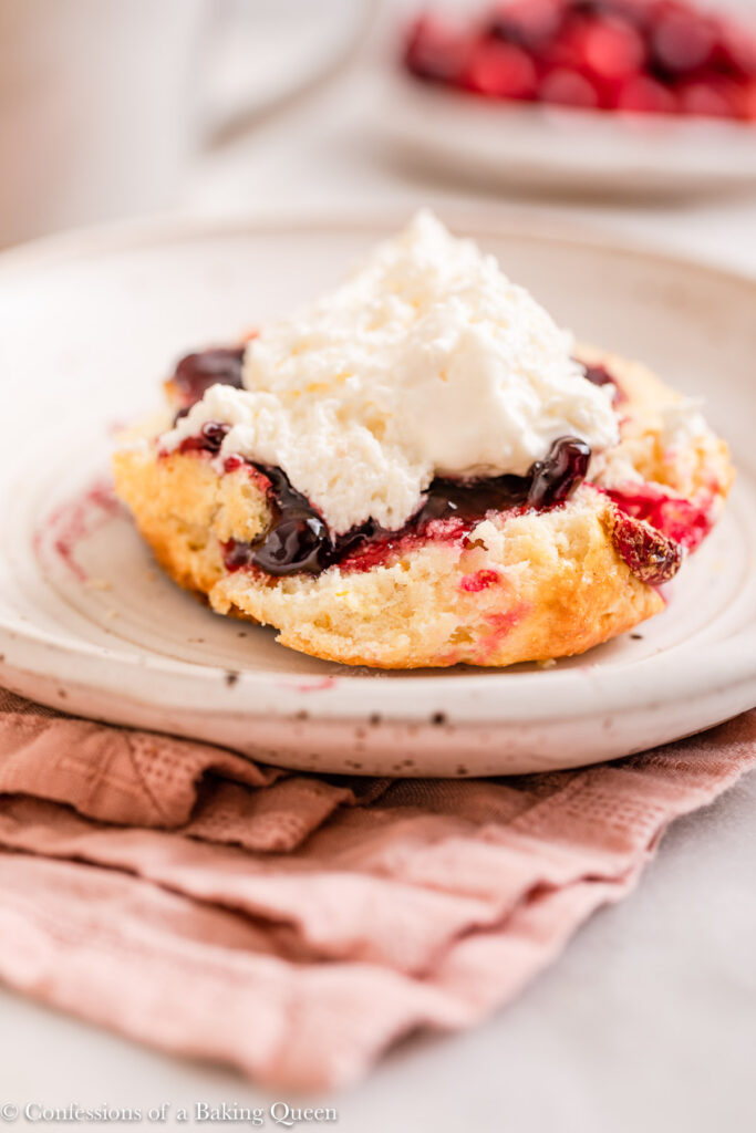 orange cranberry scone topped with jam and cream on a white plate on top of a pink linen on a white marble surface