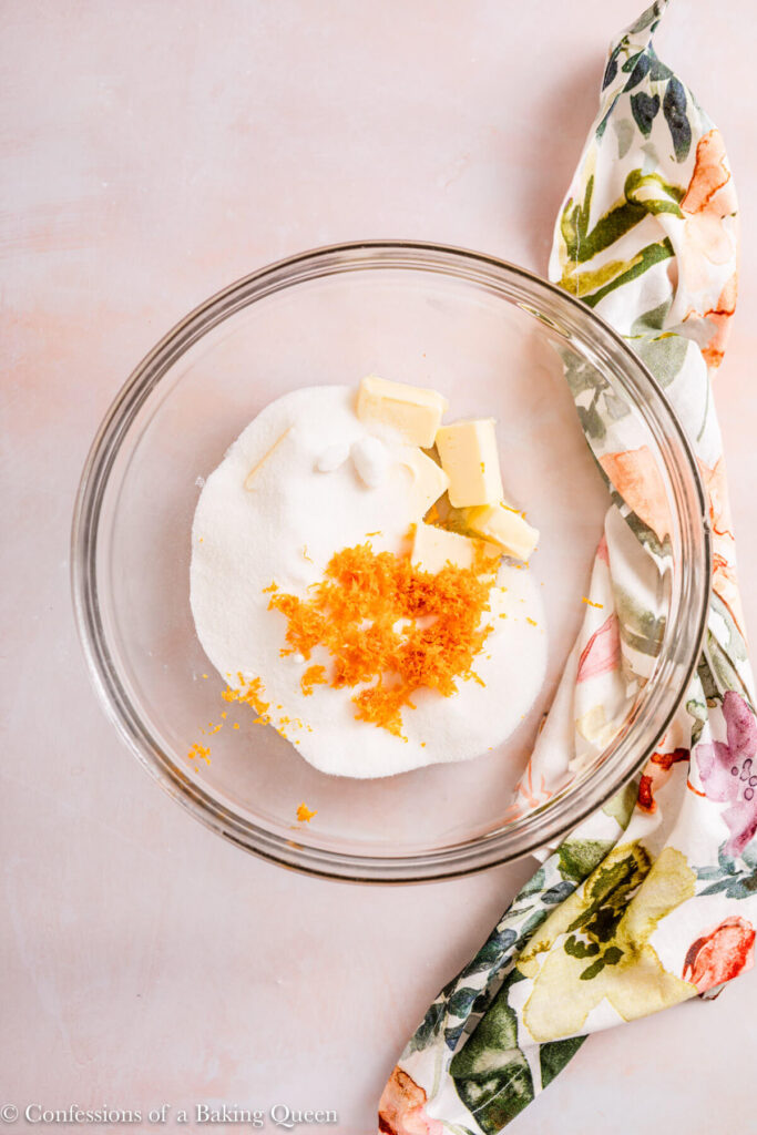 orange zest, butter, and sugar in a glass bowl on a light pink surface with a floral linen