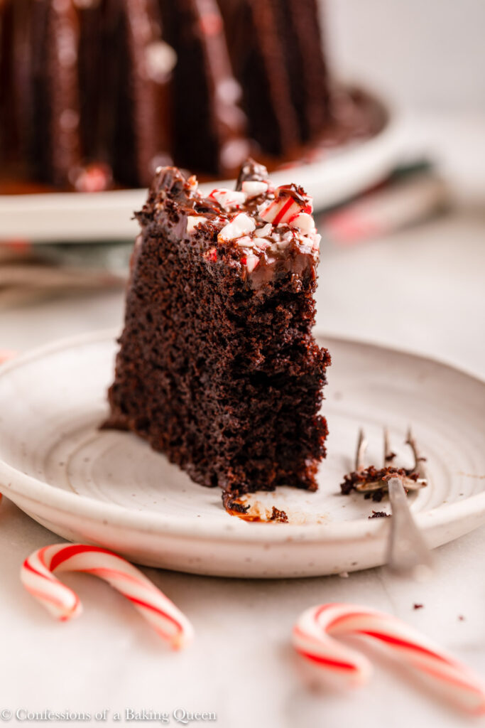 half eaten slice of peppermint chocolate cake on a white plate with a fork on a white marble surface with candy canes
