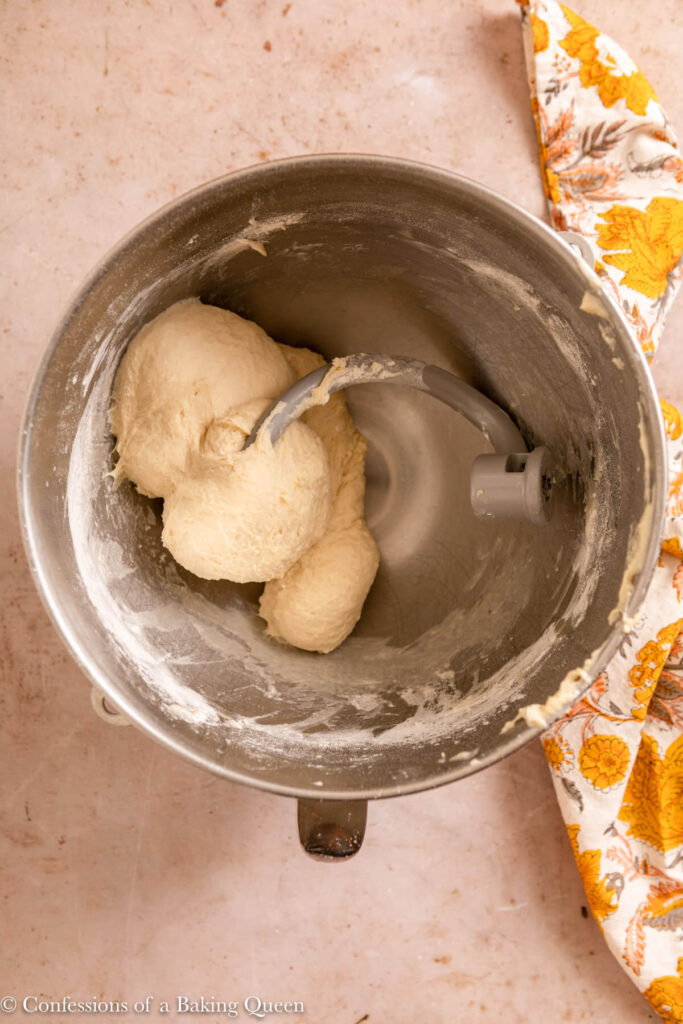 sweet dough kneaded together in a metal mixing bowl on a light brown surface with a yellow floral linen