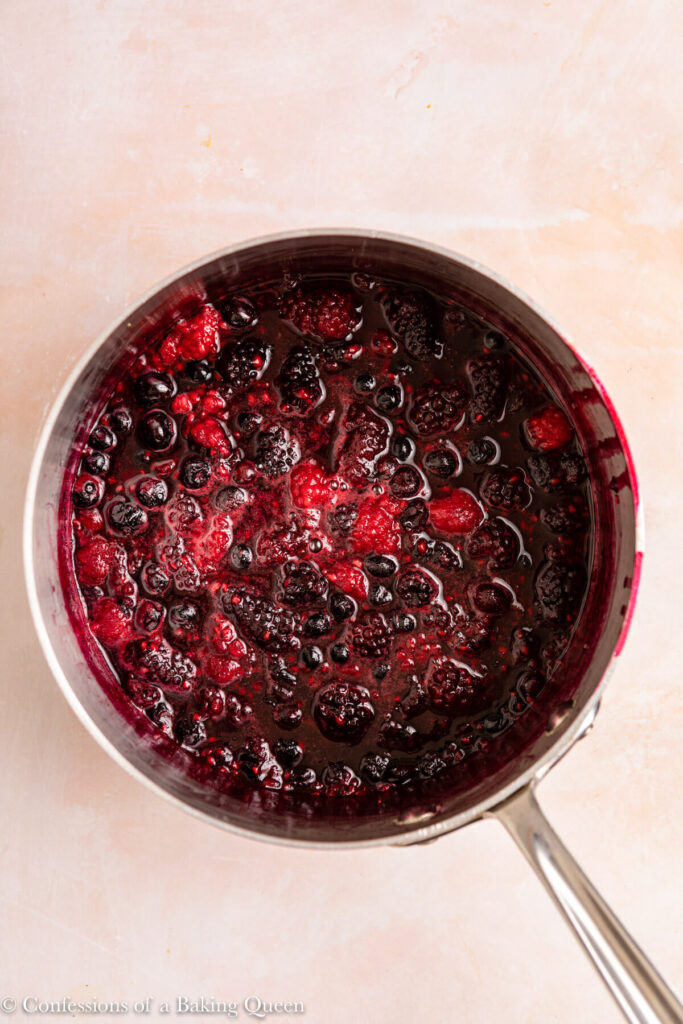 mixed berry compote cooked down in a metal pot on a light pink surface