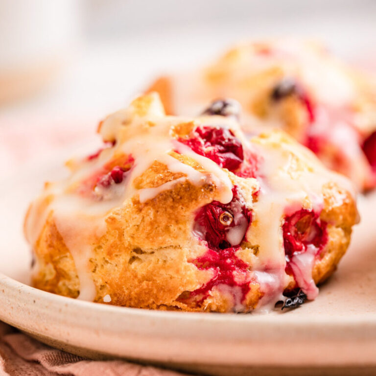 orange cranberry scone on a white plate on top of a pink linen on a white marble surface