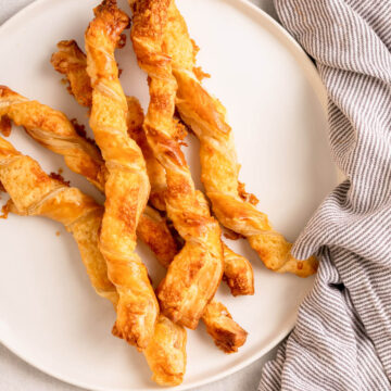 puff pastry cheese straws served on a white plate with a blue and white linen on a light grey surface