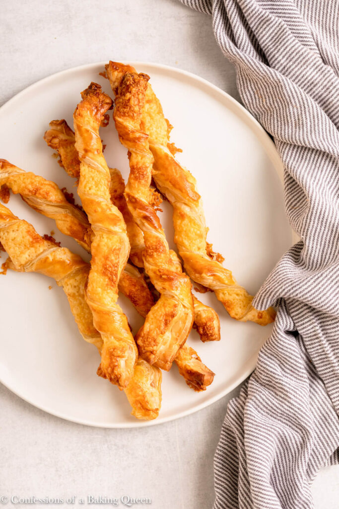 puff pastry cheese straws served on a white plate with a blue and white linen on a light grey surface