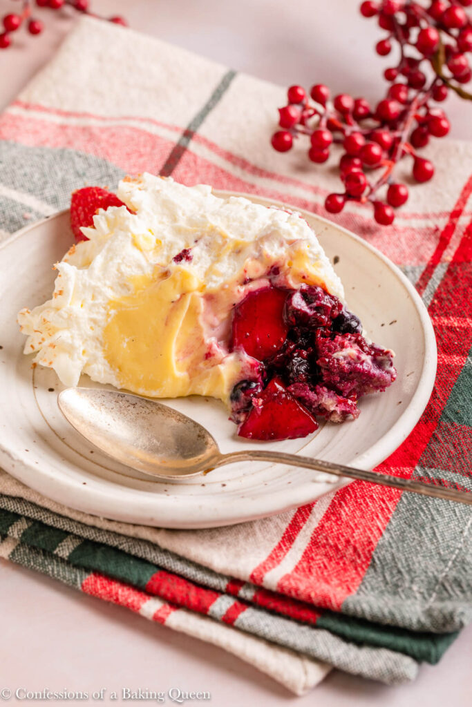 scoop of english trifle served on a white plate with a spoon on a christmas linen with christmas berries