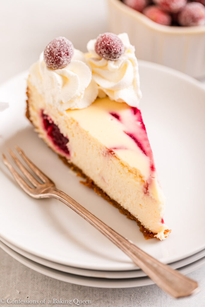 slice of white chocolate cranberry swirled cheesecake on a white plate on a light grey surface