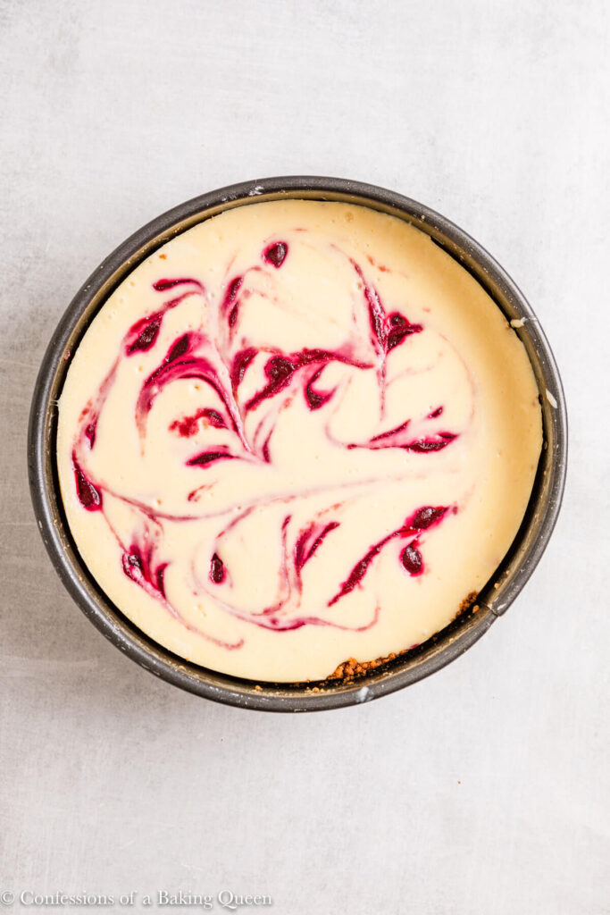 white chocolate cranberry cheesecake in a springform pan on a light grey surface