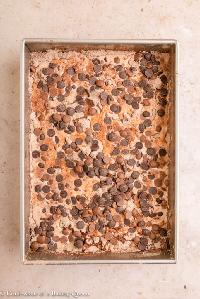 chocolate chips added on top of cake ingredients in a metal cake pan on a light brown surface